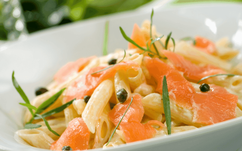 Close-up of smoked salmon pasta with fresh dill and lemon zest on a rustic plate