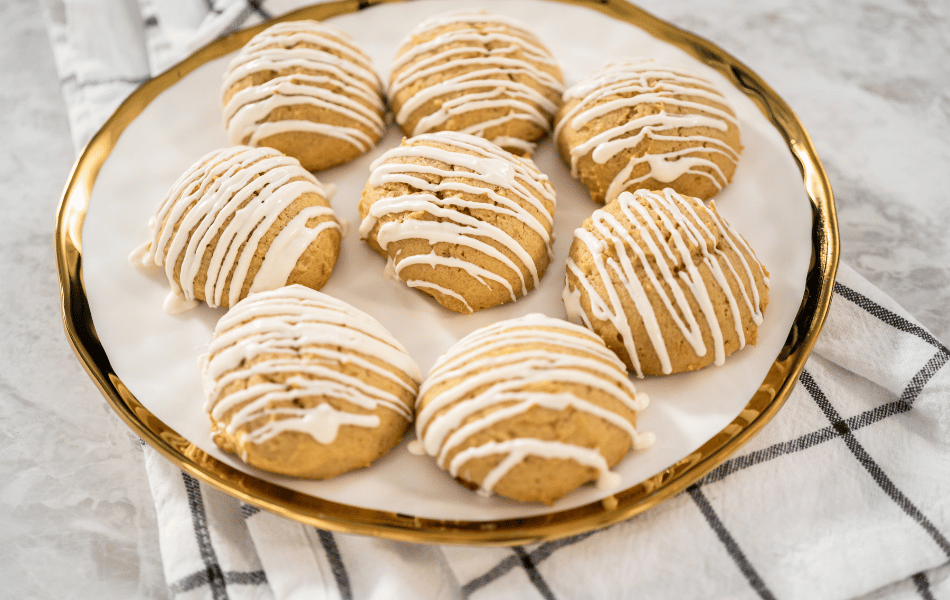 "Iced Pumpkin Cookies with vanilla icing and fall spices on a rustic wooden board.