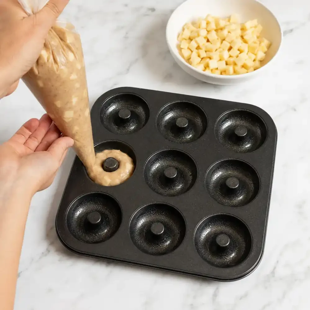 Piping apple donut batter into a greased donut pan