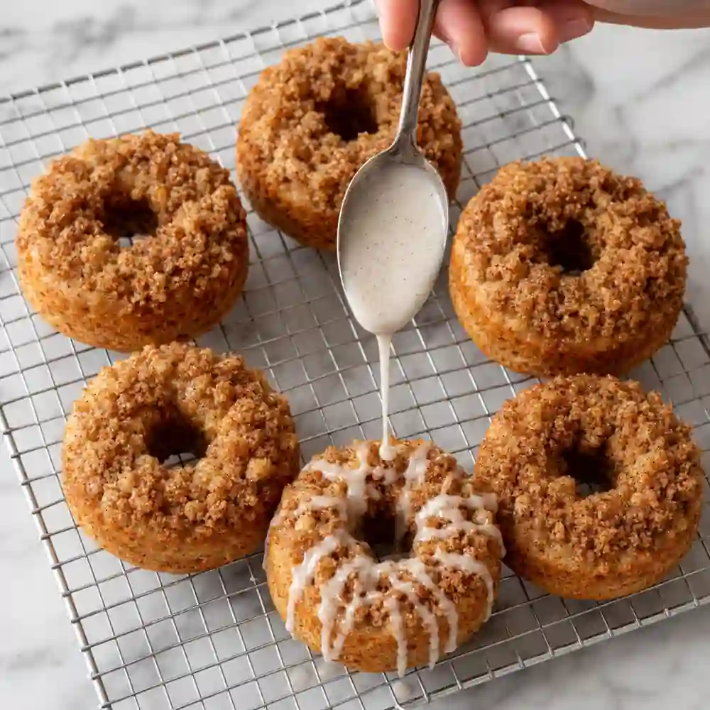 Drizzling cinnamon icing over cooled apple crumble baked donuts